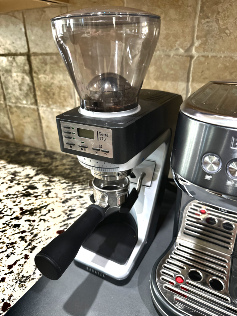 Baratza Sette 270 espresso grinder with portafilter attached, positioned next to a Bambino Plus espresso machine on a kitchen counter.