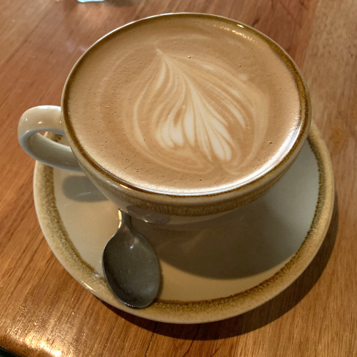 Latte with leaf latte art in a beige cup and saucer on a wooden table