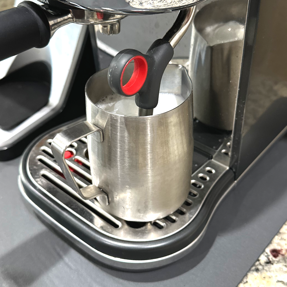Steam wand frothing milk in a stainless steel pitcher on an espresso machine